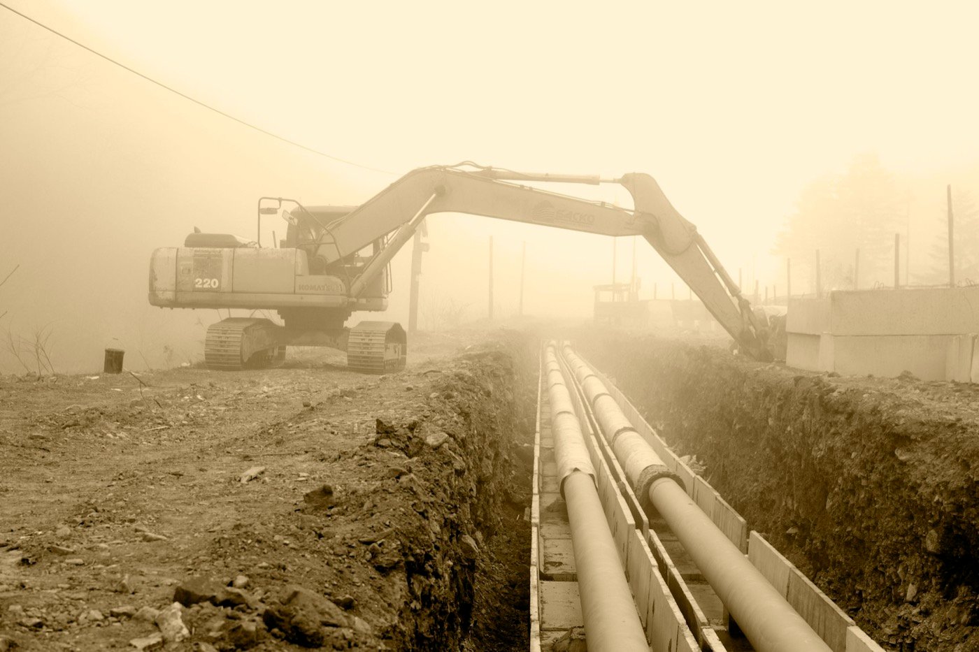 Bagger an einem Graben mit verlegten Rohren